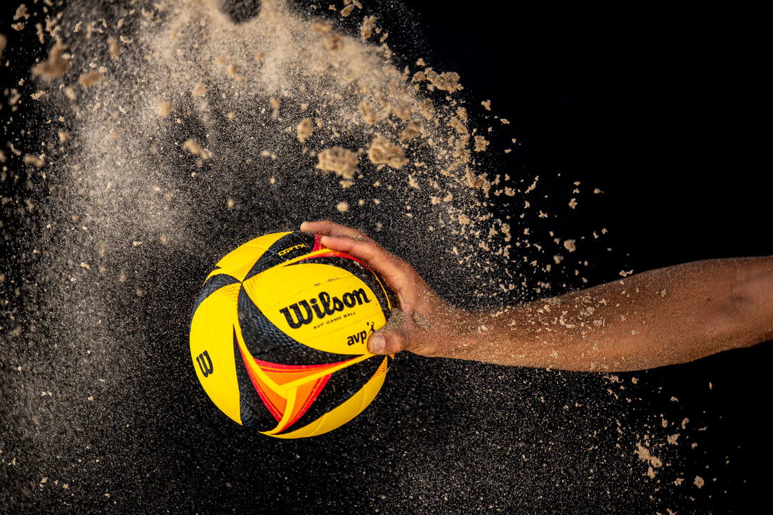 Player gripping a Wilson volleyball with sand flying, showcasing the excitement of the AVP 2026 schedule.